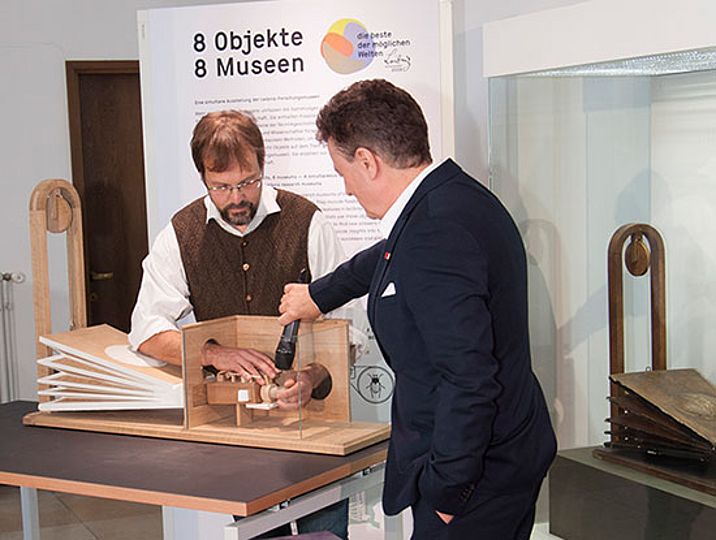 Alexander Steinbeißer, lässt den Nachbau "sprechen". Generaldirektor Heckl hält ein Mikrofon an den Sprechapparat..