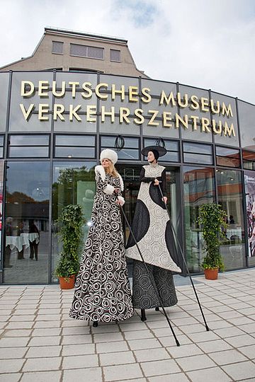 Zwei Damen auf Stelzen vor dem Haupteingang des Verkehrszentrums.