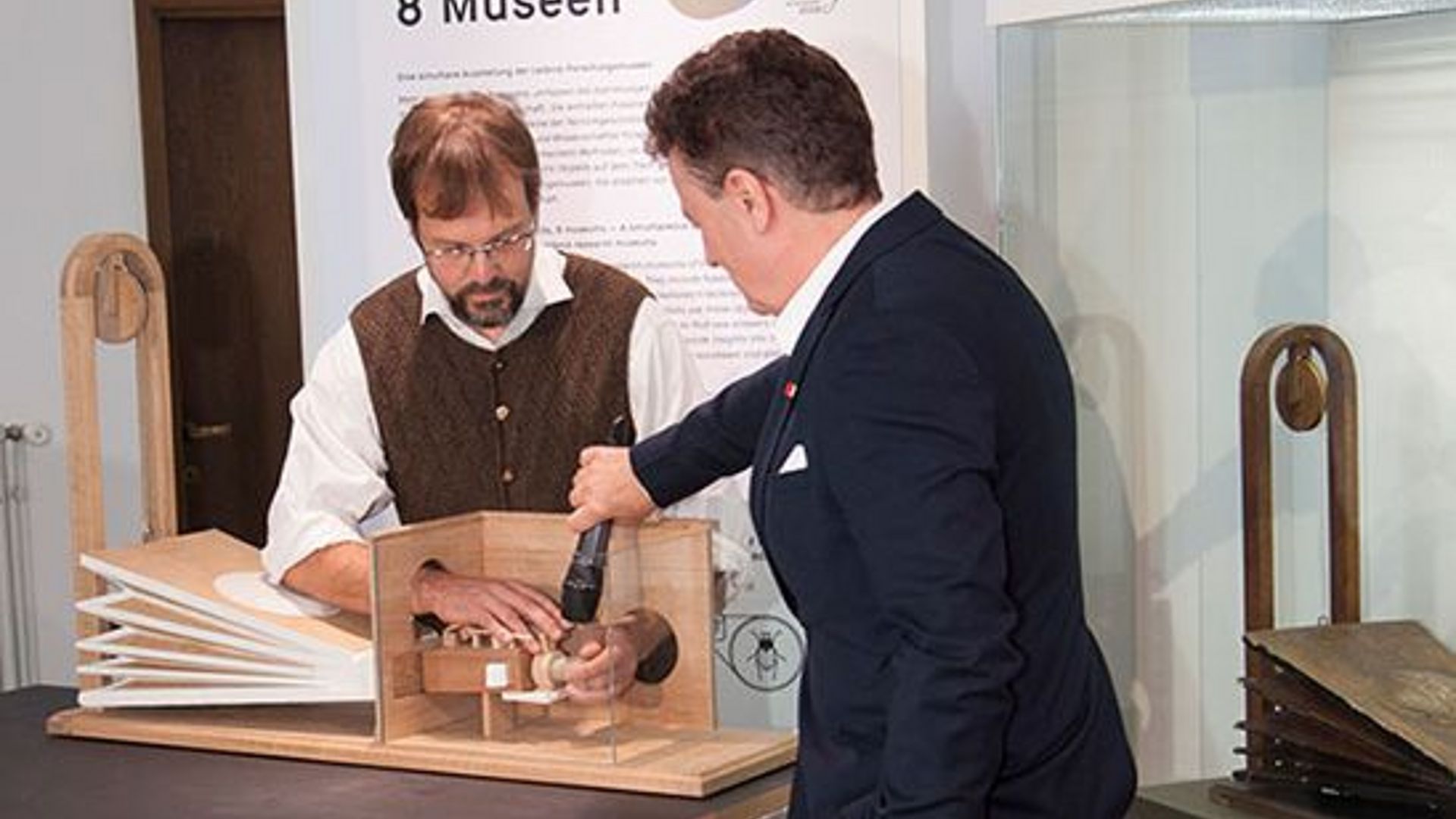 Alexander Steinbeißer, lässt den Nachbau "sprechen". Generaldirektor Heckl hält ein Mikrofon an den Sprechapparat..